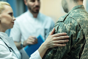 Close up of army soldier being consoled while talking with doctors at clinic