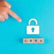 Security concept with wooden blocks, paper lock icon on blue background flat lay. man hand pointing. horizontal image