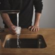 a man holding an overflowing glass of water over a running water tap