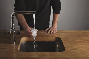 a man holding an overflowing glass of water over a running water tap