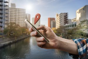 A person holding a phone in the city with a location symbol placed over the phone