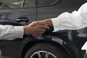 two hands shaking near a black car